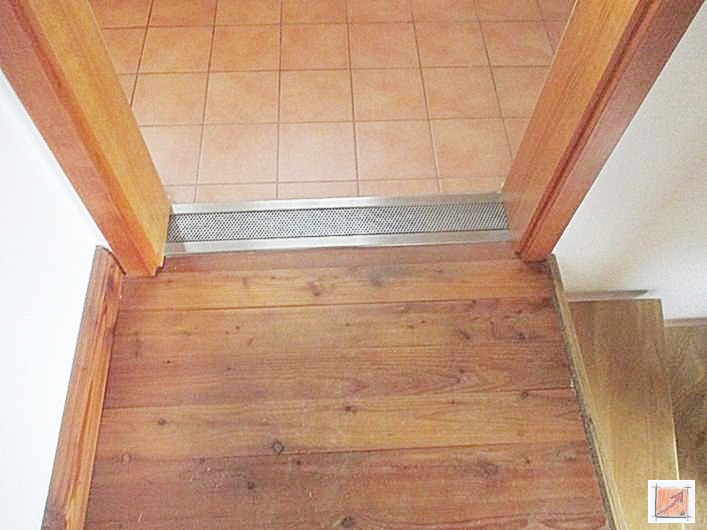 Edelstahlrinne als Übergang zwischen Badfliesen und massiven Douglasie-Holzdielen im Holzhaus.